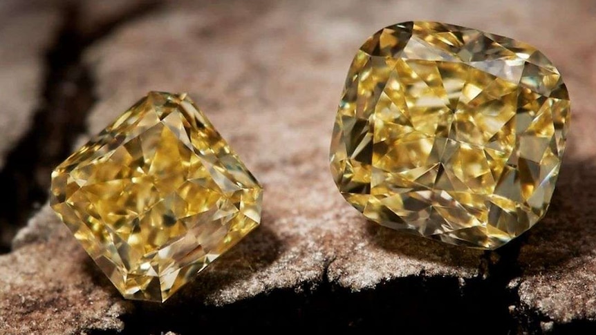 A close up of three yellow diamonds sitting on a rock