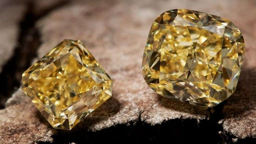 A close up of three yellow diamonds sitting on a rock.