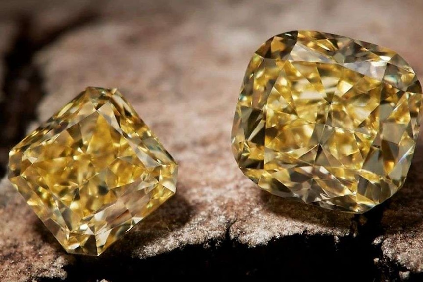 A close up of three yellow diamonds sitting on a rock.
