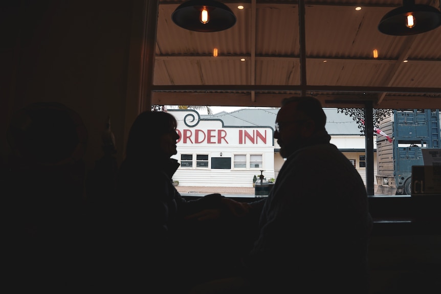 The silhouette of a man and woman sitting at a cafe window bench.