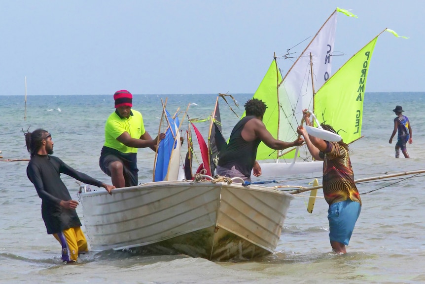 A group of men unload model boats out of a tinny