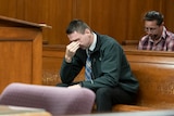A man sits in court with his head in his hand. 