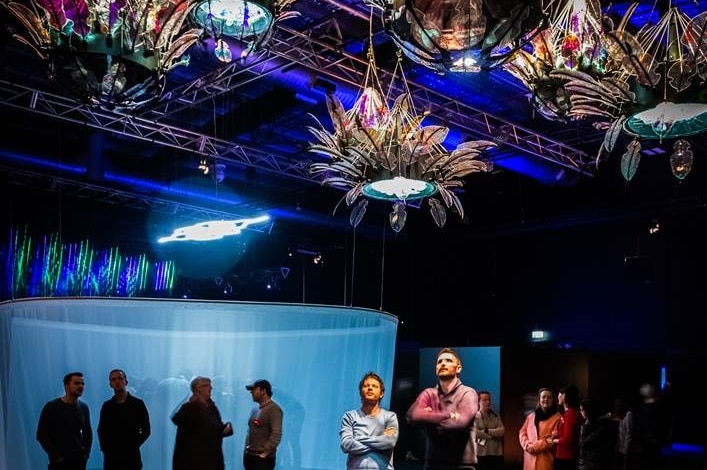 A large lit art work, depicting coloured flower sculptures, hanging from the ceiling.