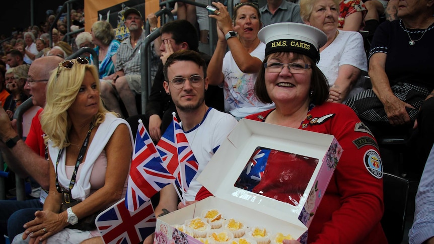 Kath Ryan sitting in crowd, showing off her vanilla butterfly cakes.