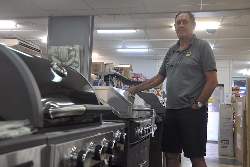 A man in a grey shirt stands next to three barbeques.