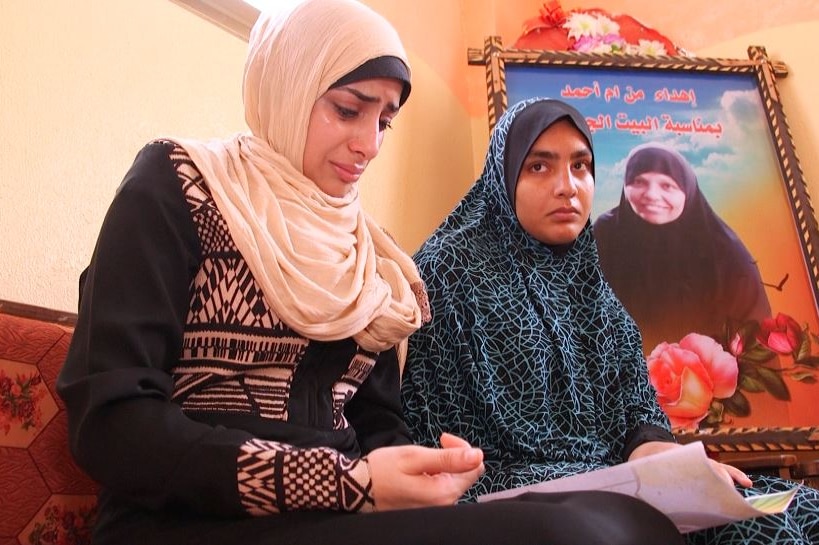 Two women sit on a couch and one cries while looking at a photograph.