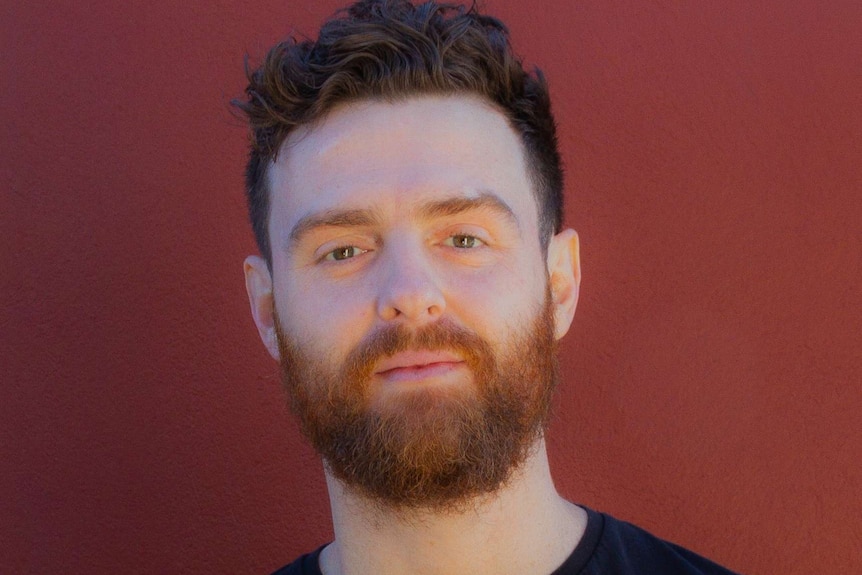 Picture of a man in a black T-shirt against a red background.