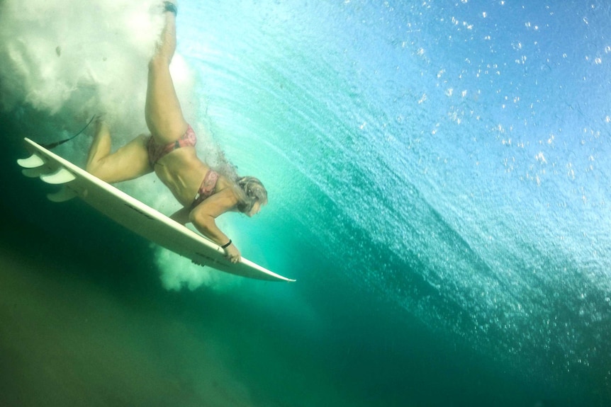 View from under the water of a surfer diving under the waves with her surfboard.