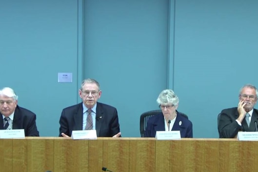 Four people sititing at a bench at the royal commission, with a blue background.