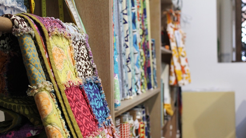 Quilt hanging on a shelf filled with colourful fabric and measuring tapes.