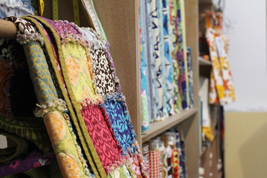 Quilt hanging on a shelf filled with colourful fabric and measuring tapes.