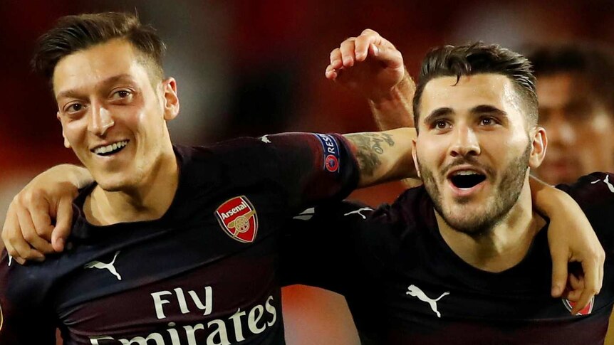 Arsenal's Mesut Ozil, Sead Kolasinac and Sokratis Papastathopoulos have their arms over each others' shoulders.
