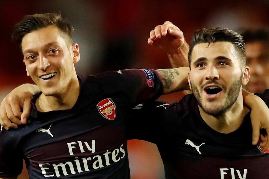 Arsenal's Mesut Ozil, Sead Kolasinac and Sokratis Papastathopoulos have their arms over each others' shoulders.