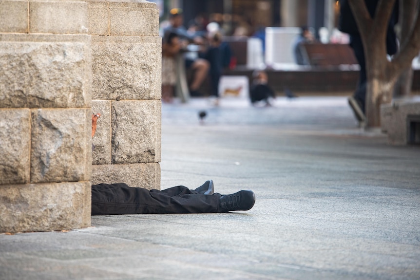 Two feet sticking out behind a wall as people walk past.