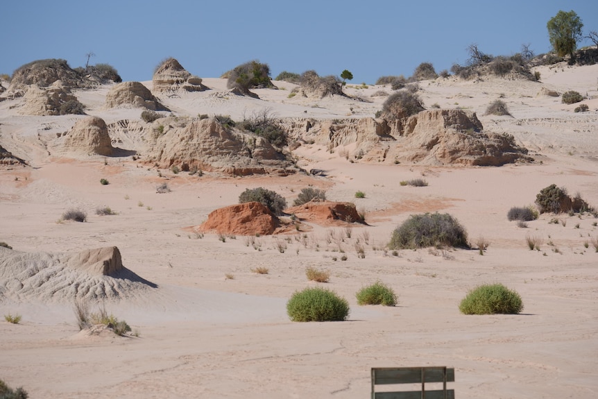 Light coloured sand featuring small rock formations and small stubble bushes