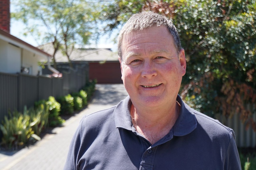 A middle aged man wearing a dark blue polo shirt smiles at the camera.