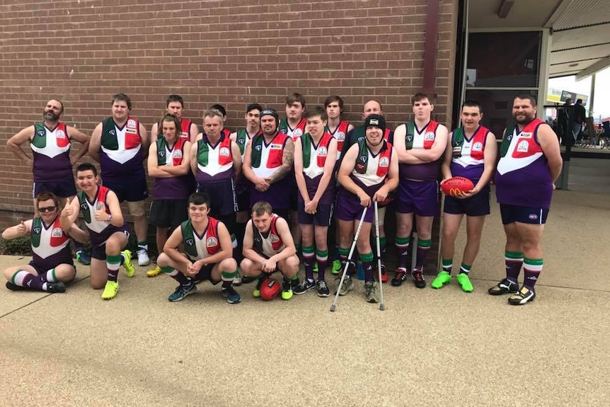 a team of Australian Rules footballers wearing their uniforms pose for a team photo.