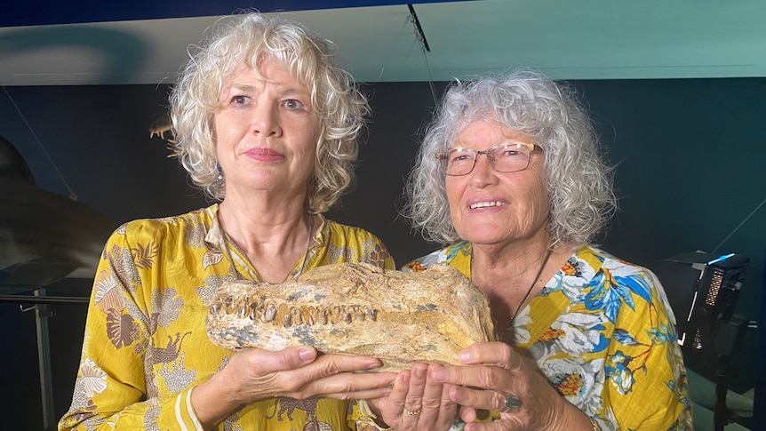 Two woman hold fossil skeleton and look at camera