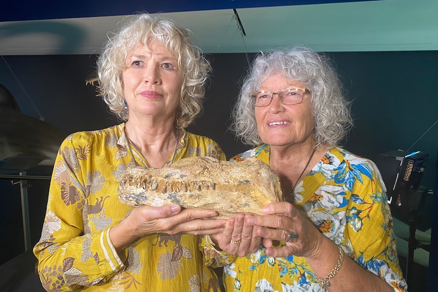 Two woman hold fossil skeleton and look at camera