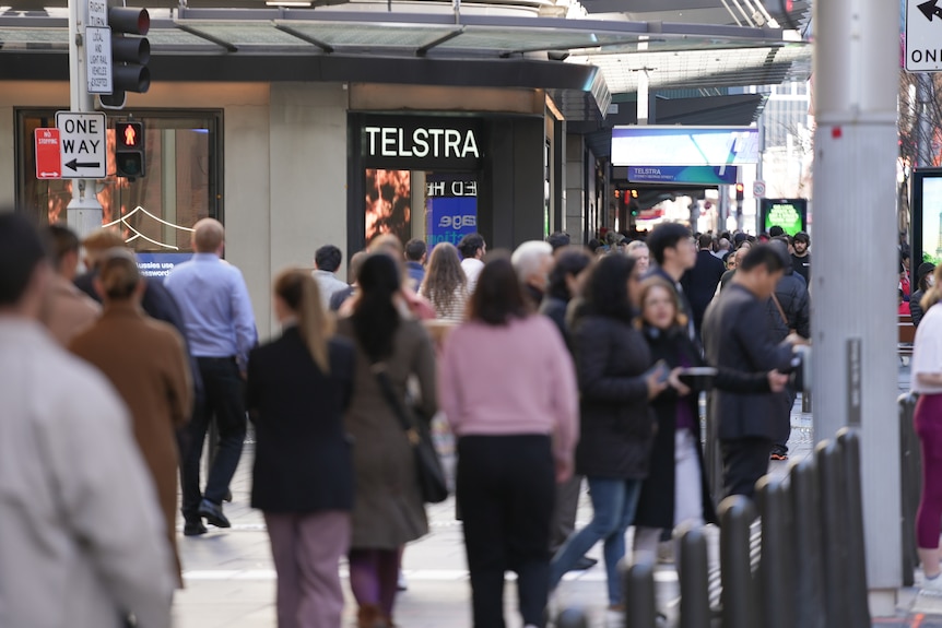 a crowd walks past a Telstra store