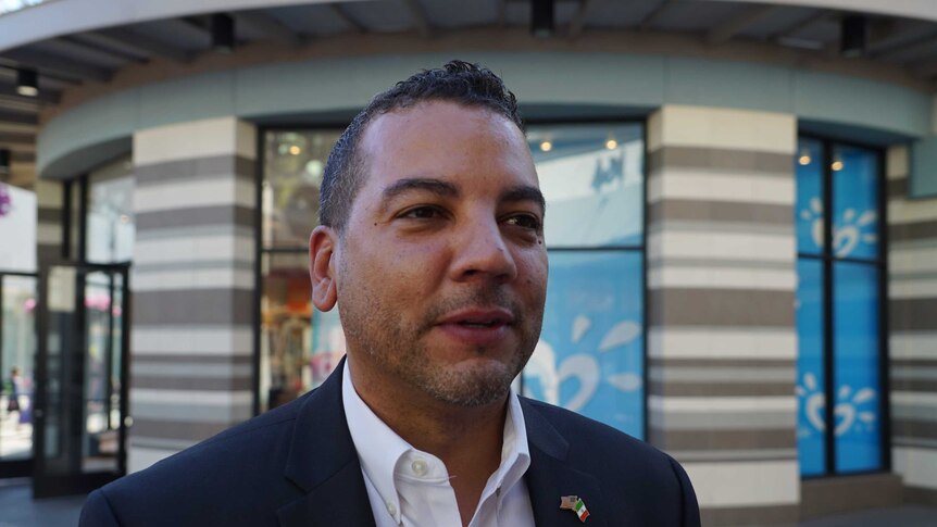 Headshot of Jason Wells who wears a suit and stands in front of shops