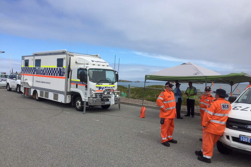 SES volunteers stand next to a mobile police command centre, near the beach.