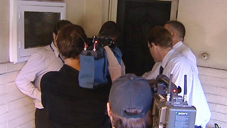 Journalists and cameramen crowd around the front door of a house.
