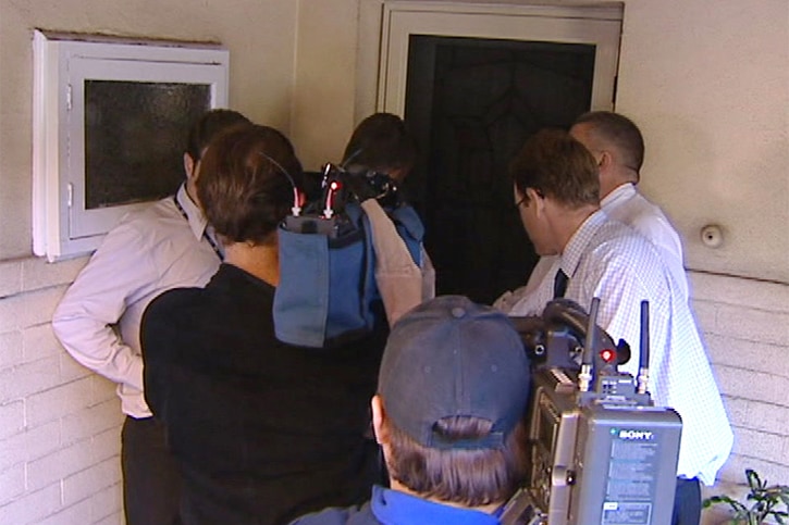 Journalists and cameramen crowd around the front door of a house.