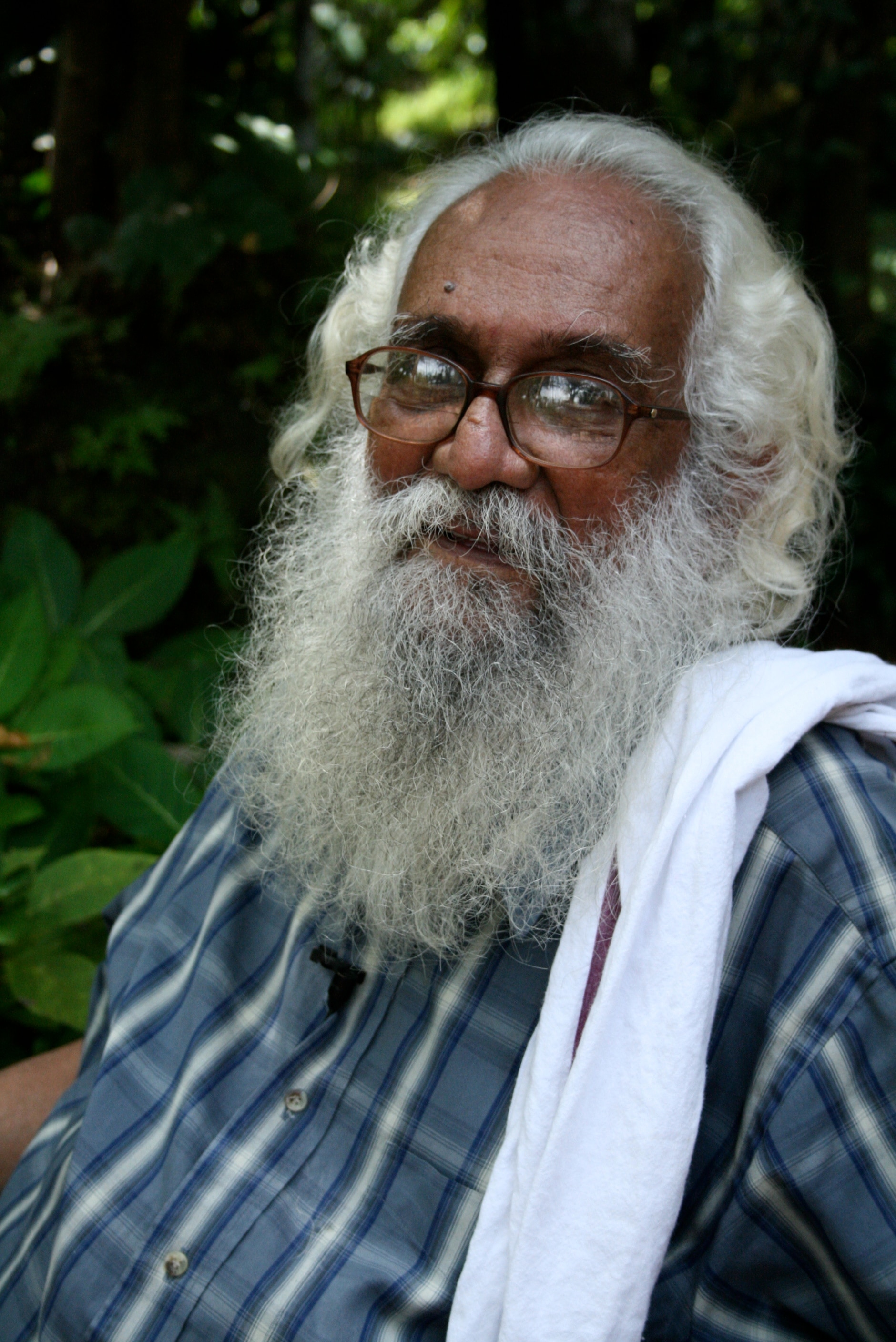 A man with long white hair and white beard, with glasses, smiles at the camera.