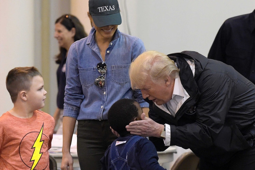 Donald Trump bends down to cup the face of a little boy while Melania, wearing a cap that says TEXAS, looks on