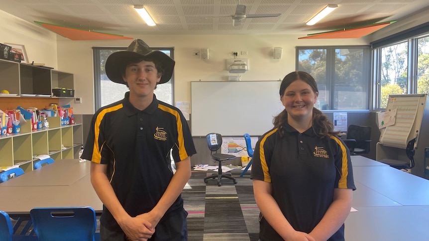 Two teenage students in navy and yellow uniforms standing in a classroom. 