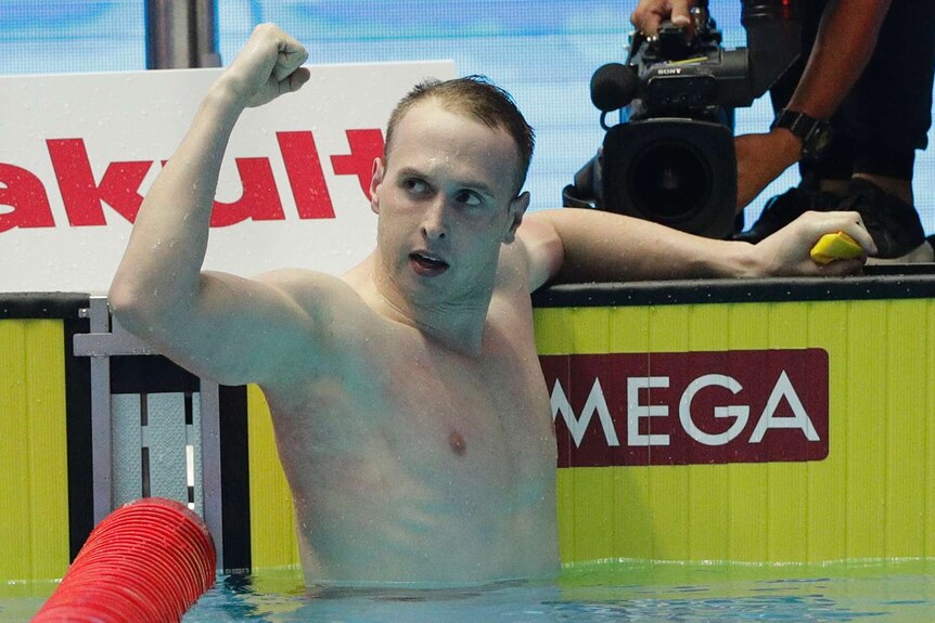A male swimmer pumps his right fist while standing at the wall at the end of the pool.