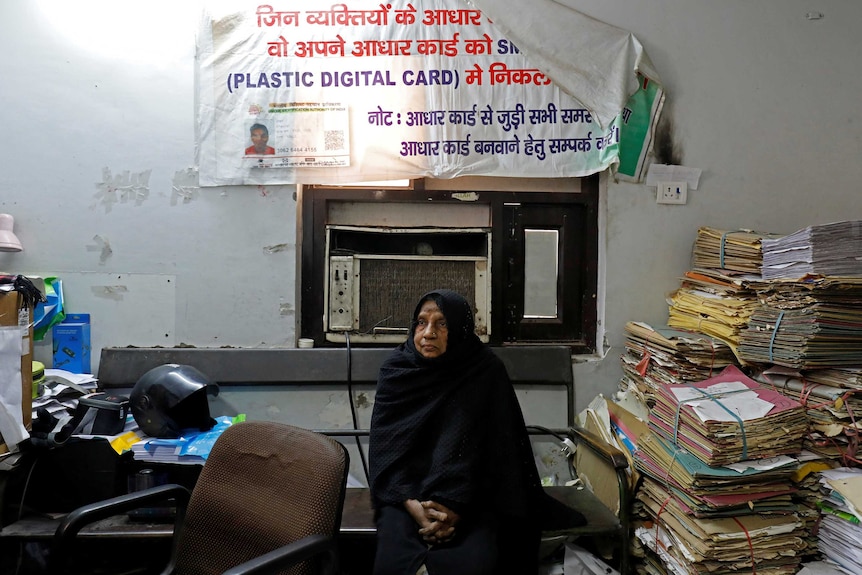 An old woman waits in an office.