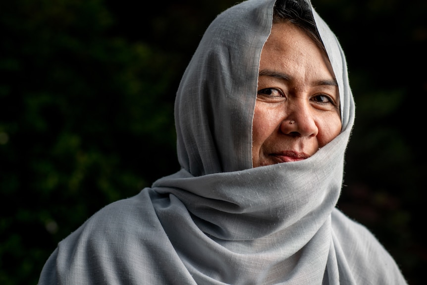 A smiling woman wearing a grey hijab