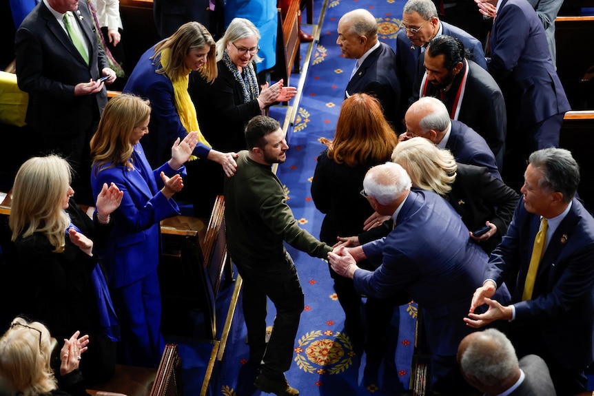 President Volodymyr Zelenskyy surrounded by several people applausing