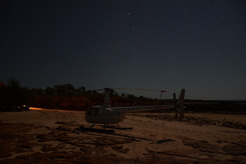 A helicopter parked on a beach under a starry night sky.