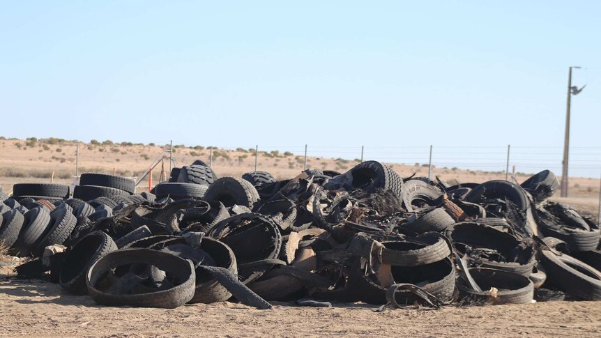 A huge pile of tyres sits on the sandy outback dirt.