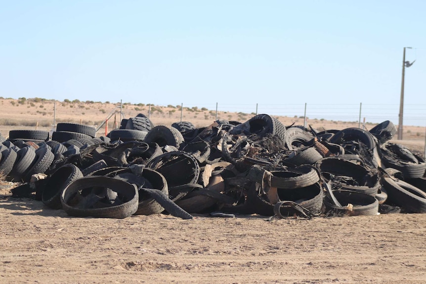 A huge pile of tyres sits on the sandy outback dirt.