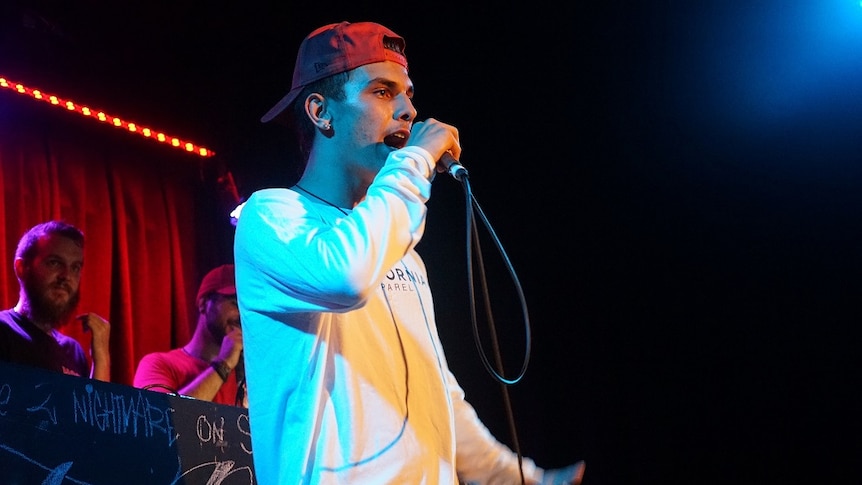 A young man is holding a microphone on stage and singing into it.