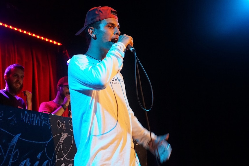 A young man is holding a microphone on stage and singing into it.