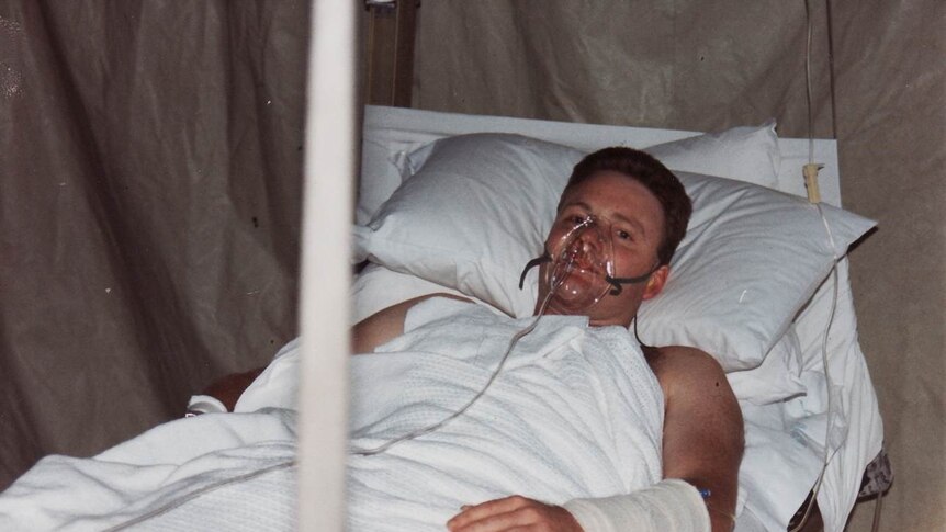 Paul Copeland lies in a hospital bed with an oxygen mask on his face.