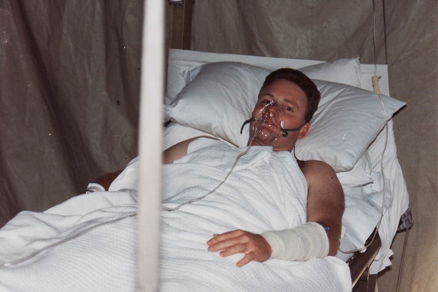 Paul Copeland lies in a hospital bed with an oxygen mask on his face.