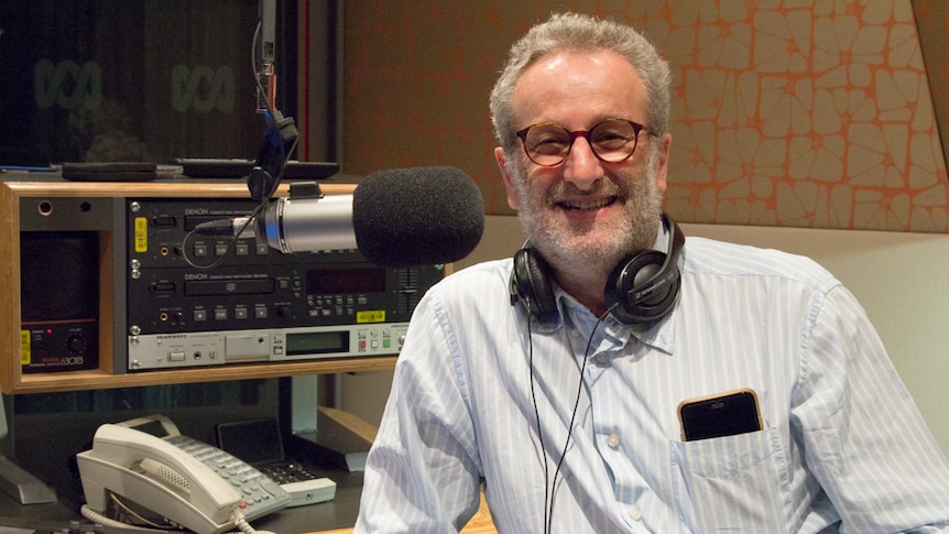 A man in a radio studio with white hair and beard smiles at the camera.