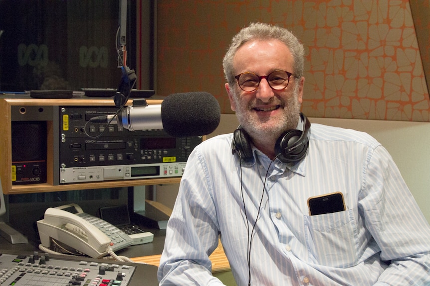 A man in a radio studio with white hair and beard smiles at the camera.