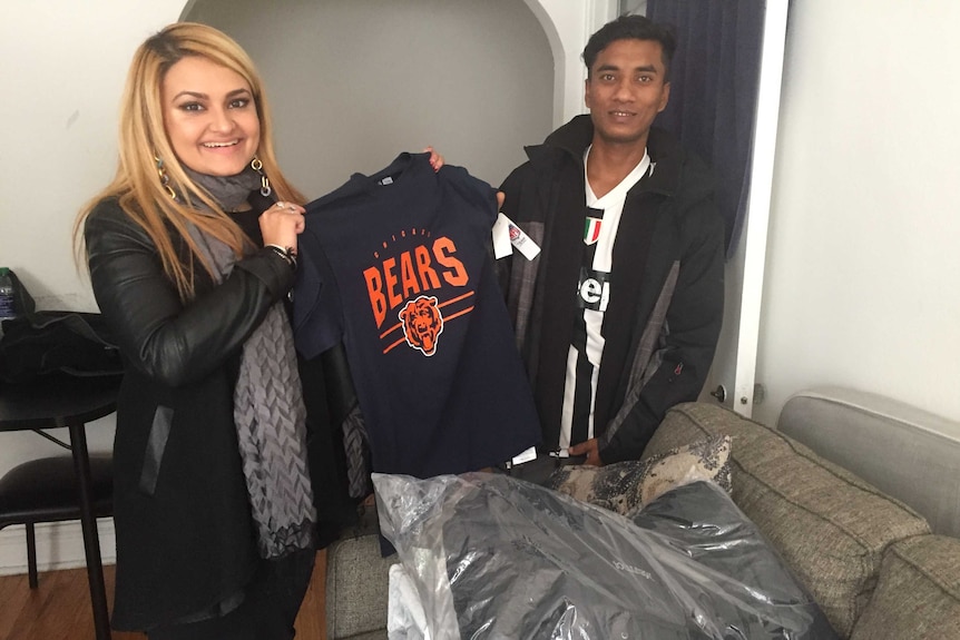 A smiling woman holds up a jumper while a man stands beside her.