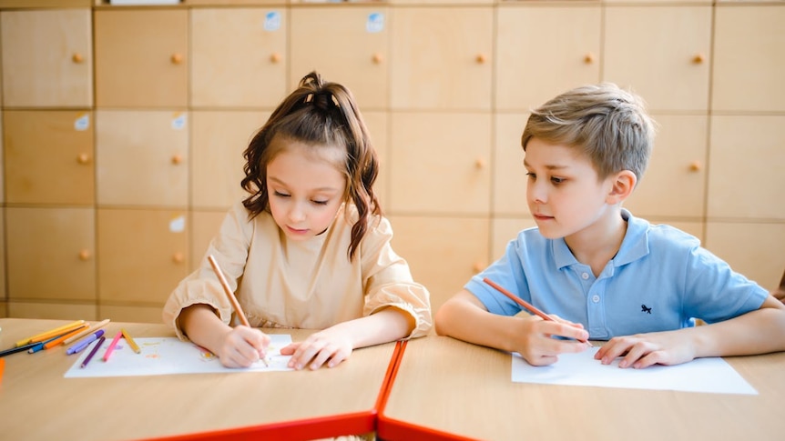Young girl and young boy sitting next to each other writing on paper