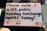 A sign on the counter of a cafe says a 15 per cent public holiday surcharge is applied.