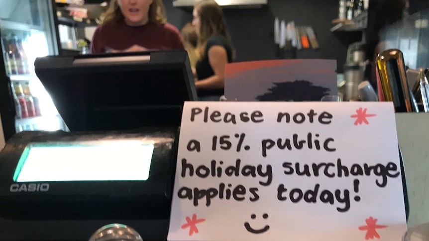 A sign on the counter of a cafe says a 15 per cent public holiday surcharge is applied.