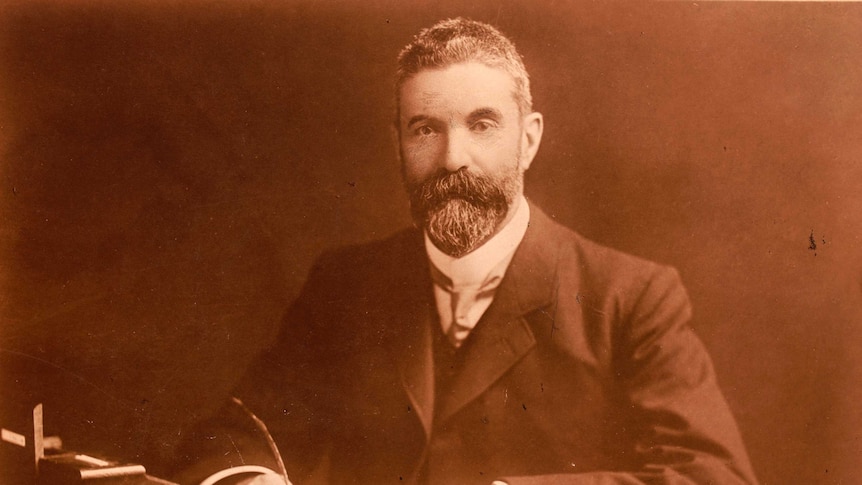 An old photo of a man with a goatee looking at a book.