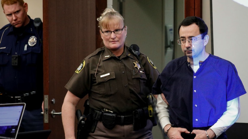 A security guard leads a shackled Larry Nasser into court